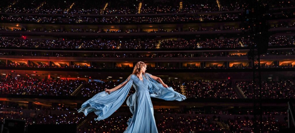 Taylor Swift singing on stage in a dark outfit during a concert performance.
